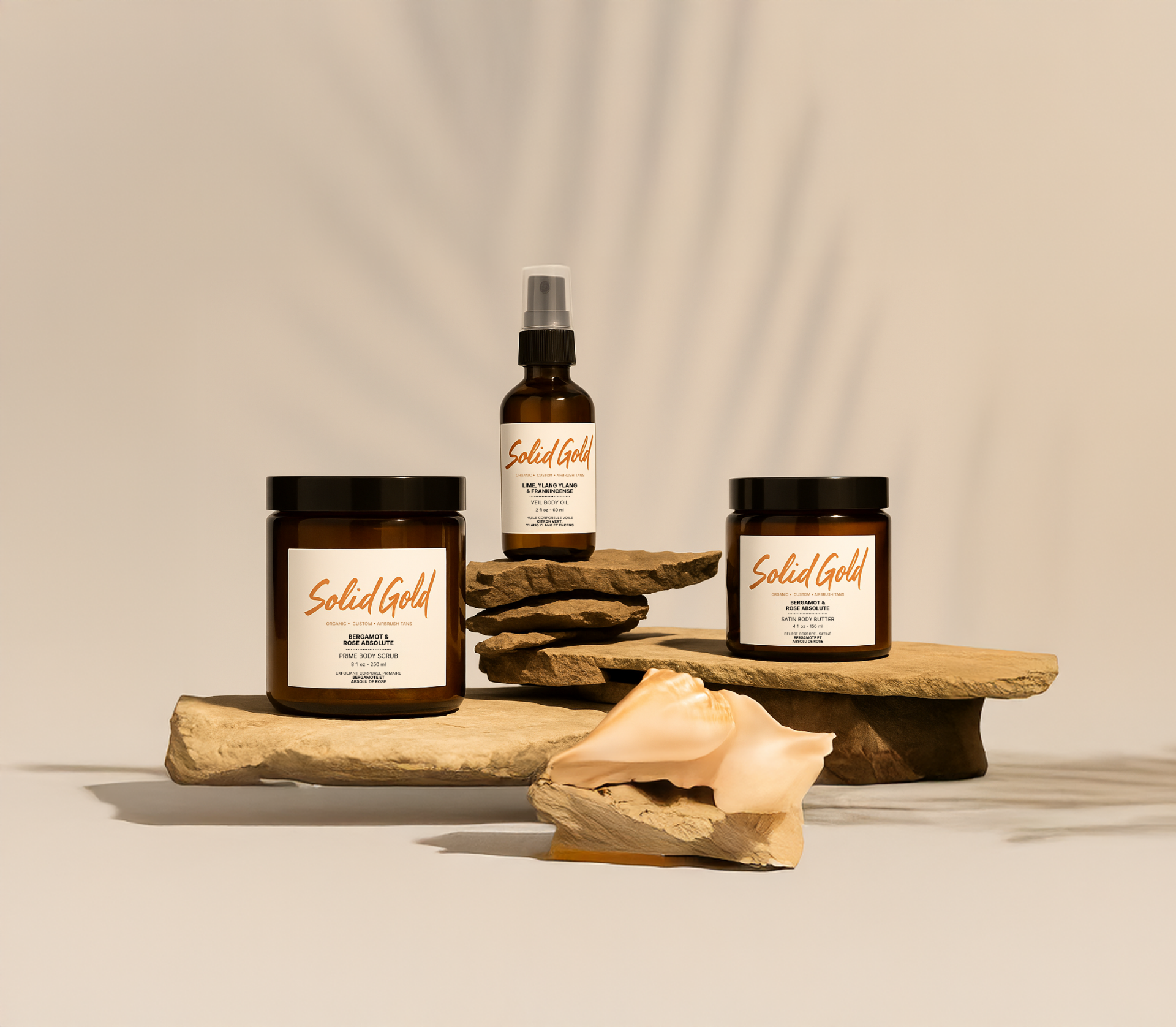 Solid Gold Complete Ritual Set — Prime Body Scrub, Veil Body Oil, and Satin Body Butter on natural stone with a seashell.