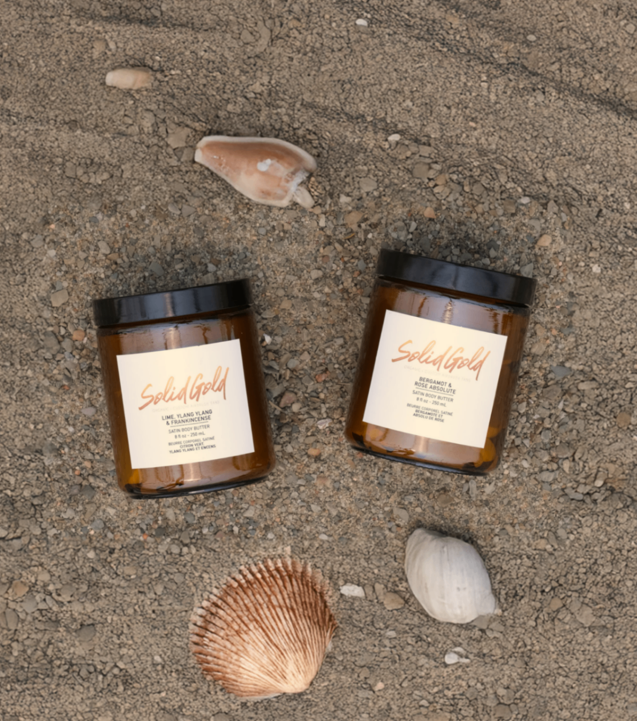 Solid Gold Prime Body Scrub jars on sand with seashells.