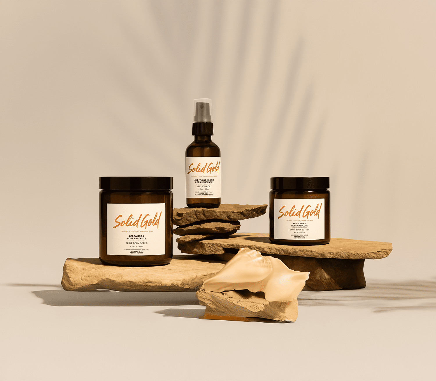 Solid Gold Ritual product line — body scrub, veil body oil, and satin body butter arranged on natural stone.